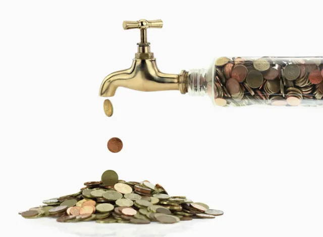 coins falling from a faucet into a glass jar