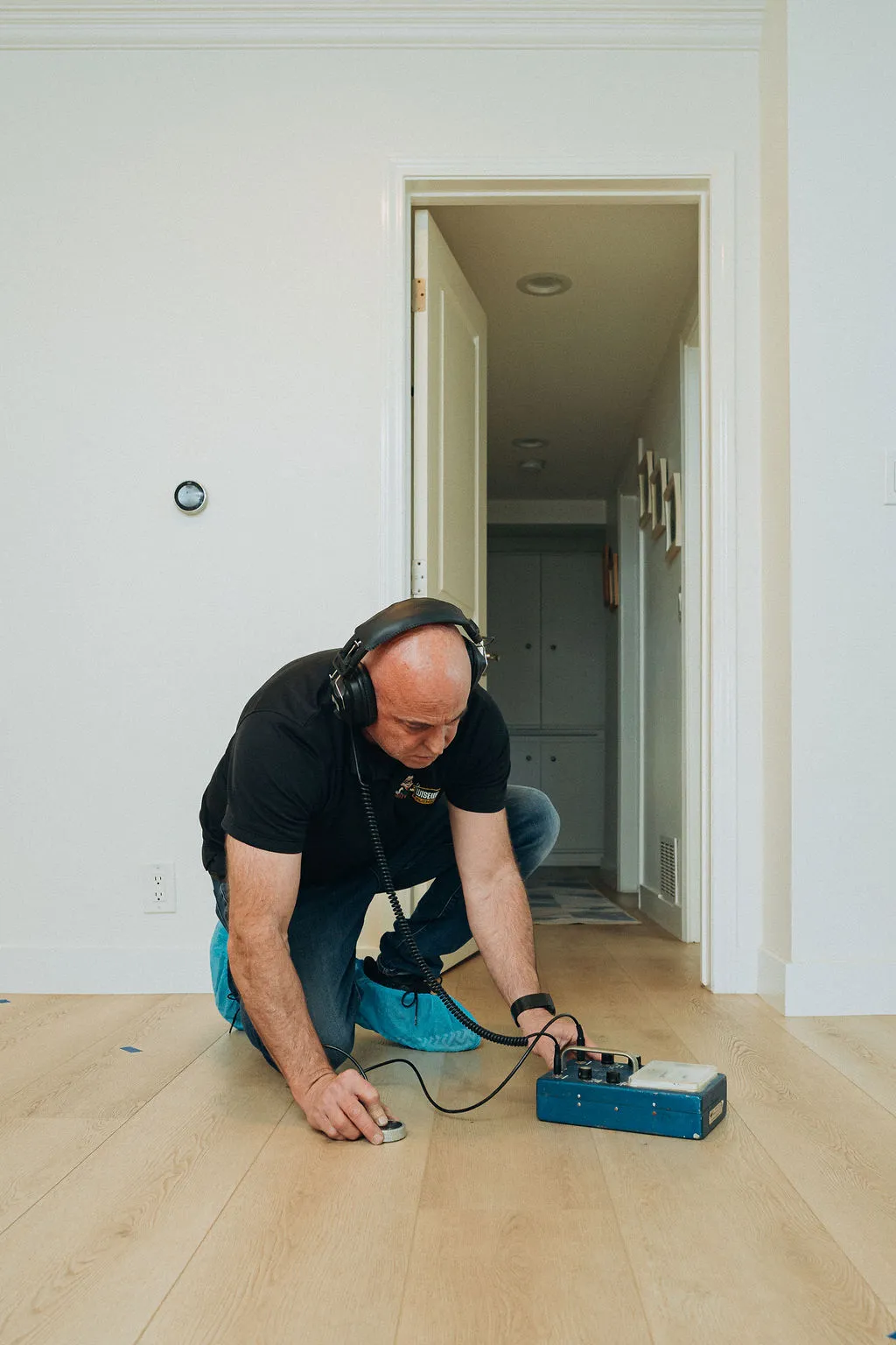 Wiseway technician using machine to test leak detection with headphones on customer's home floor